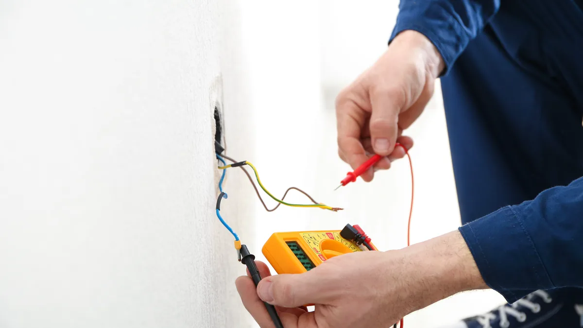 An electrician measuring earth resistance at a wall socket before installing it
