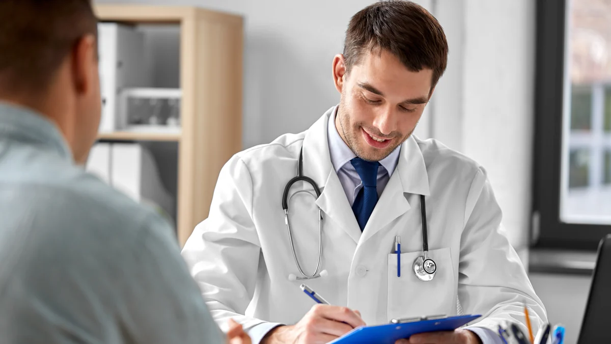 A doctor making notes on a clipboard while talking with a patient across a desk